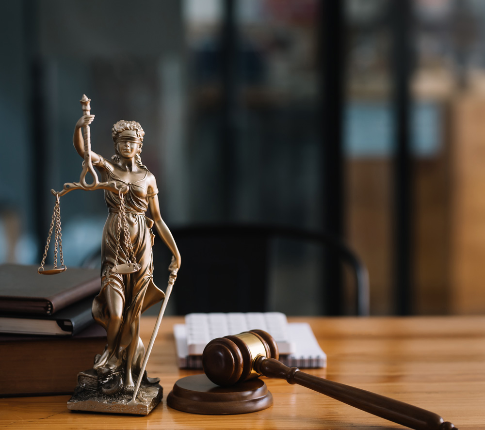 A bronze Lady Justice statue holding scales beside a wooden gavel, with law books